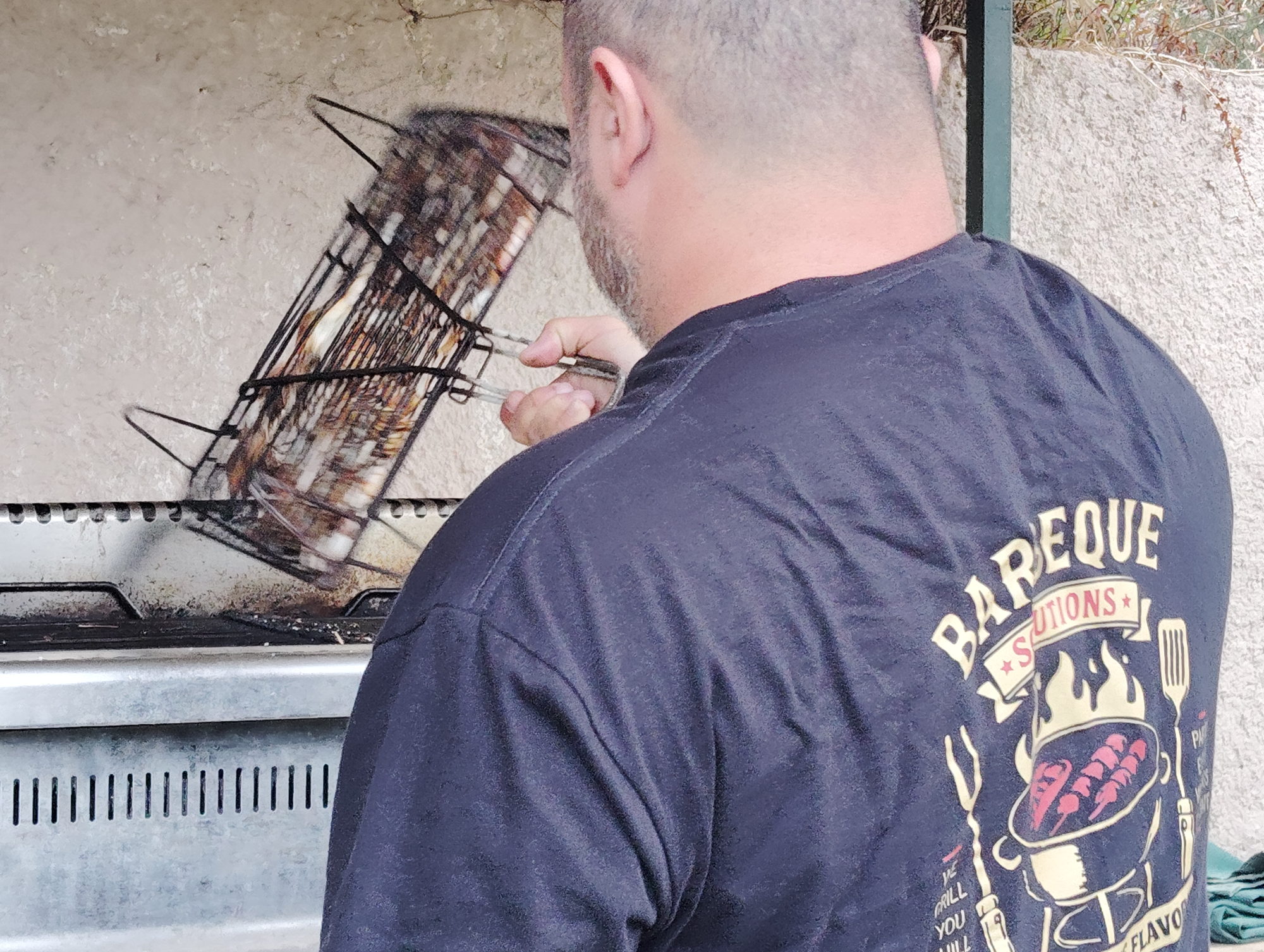 Ο σεφ με μπλούζα Barbeque Solutions σηκώνει τη σχάρα με τις γαρίδες